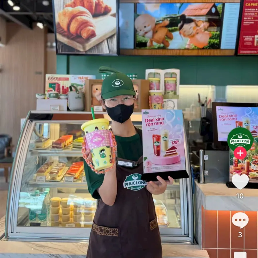 Nhân viên Phúc Long cầm ly quà 8/3 và standee Deal xinh rộn ràng tại quầy
